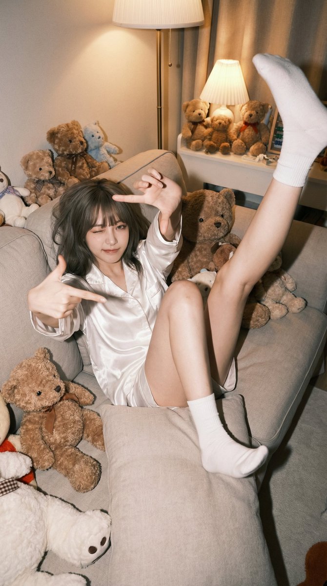 A Relaxed Young Woman in White Satin Pajamas, Playfully Kicking Leg on a Cozy Sofa in a Cute Bedroom