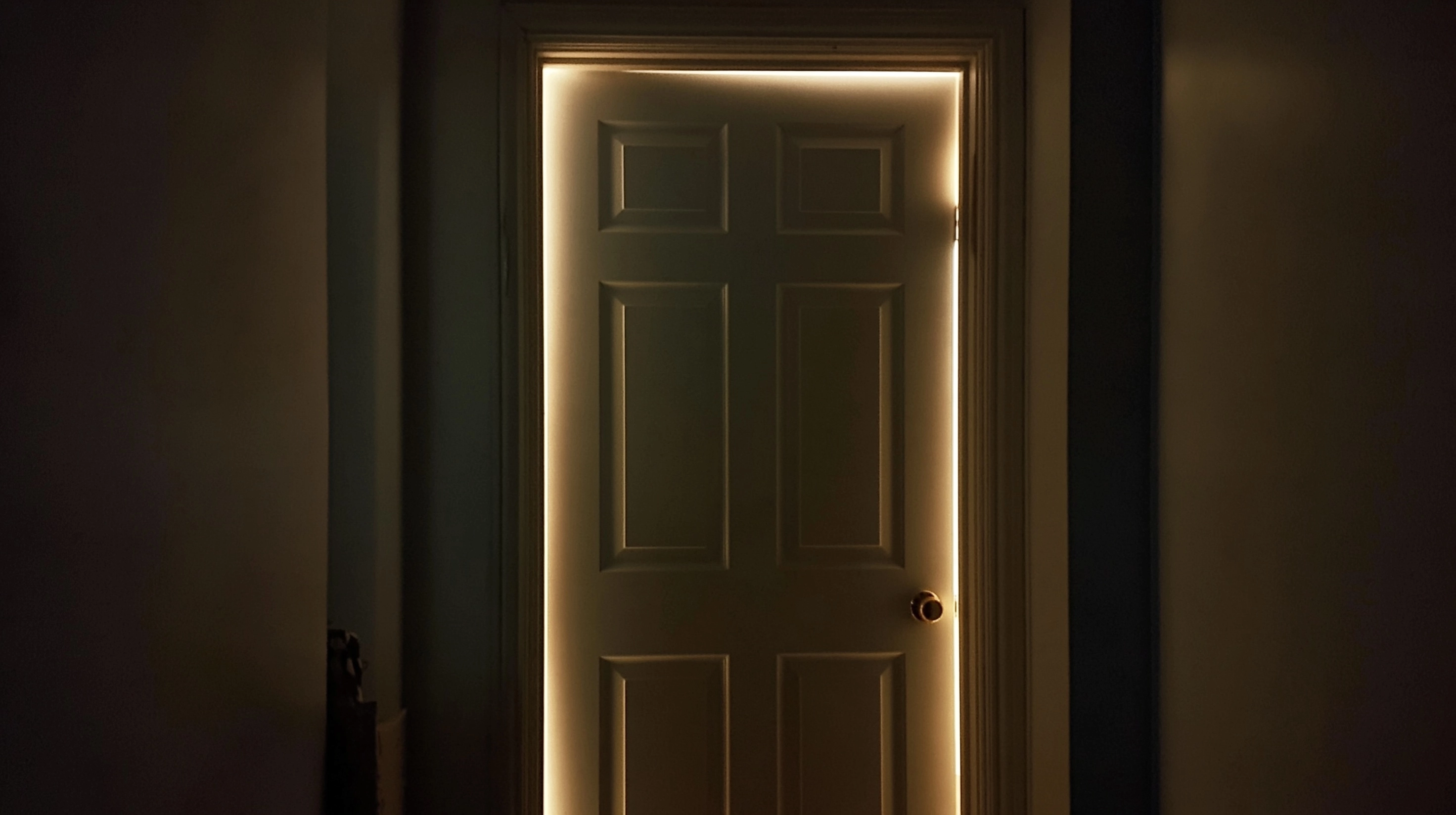 A closed bedroom door. A faint light can be traced on the door frame from the light emitted by mobil
