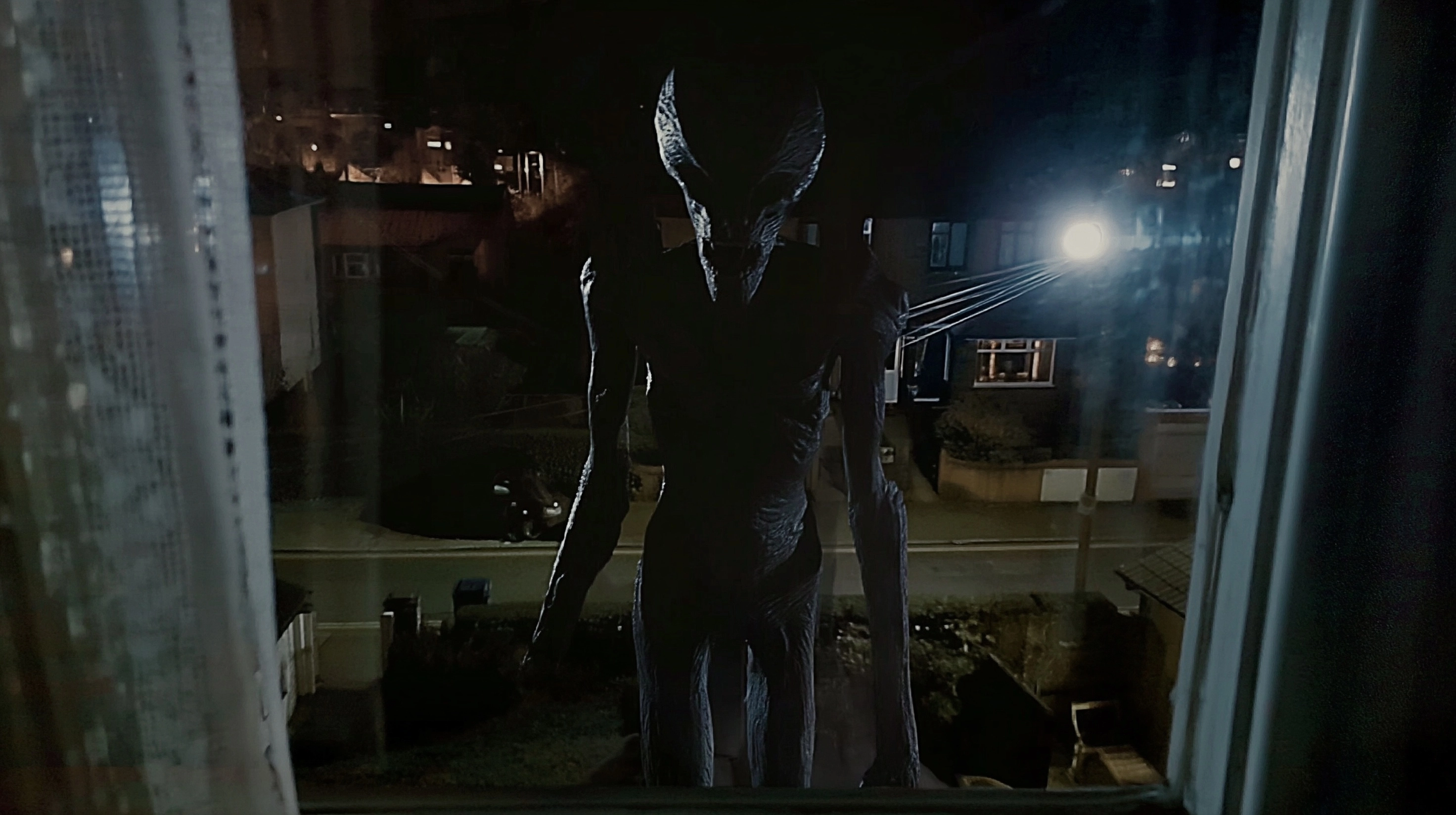 The horrifying tall lanky creature can be seen down below on the dimly lit street