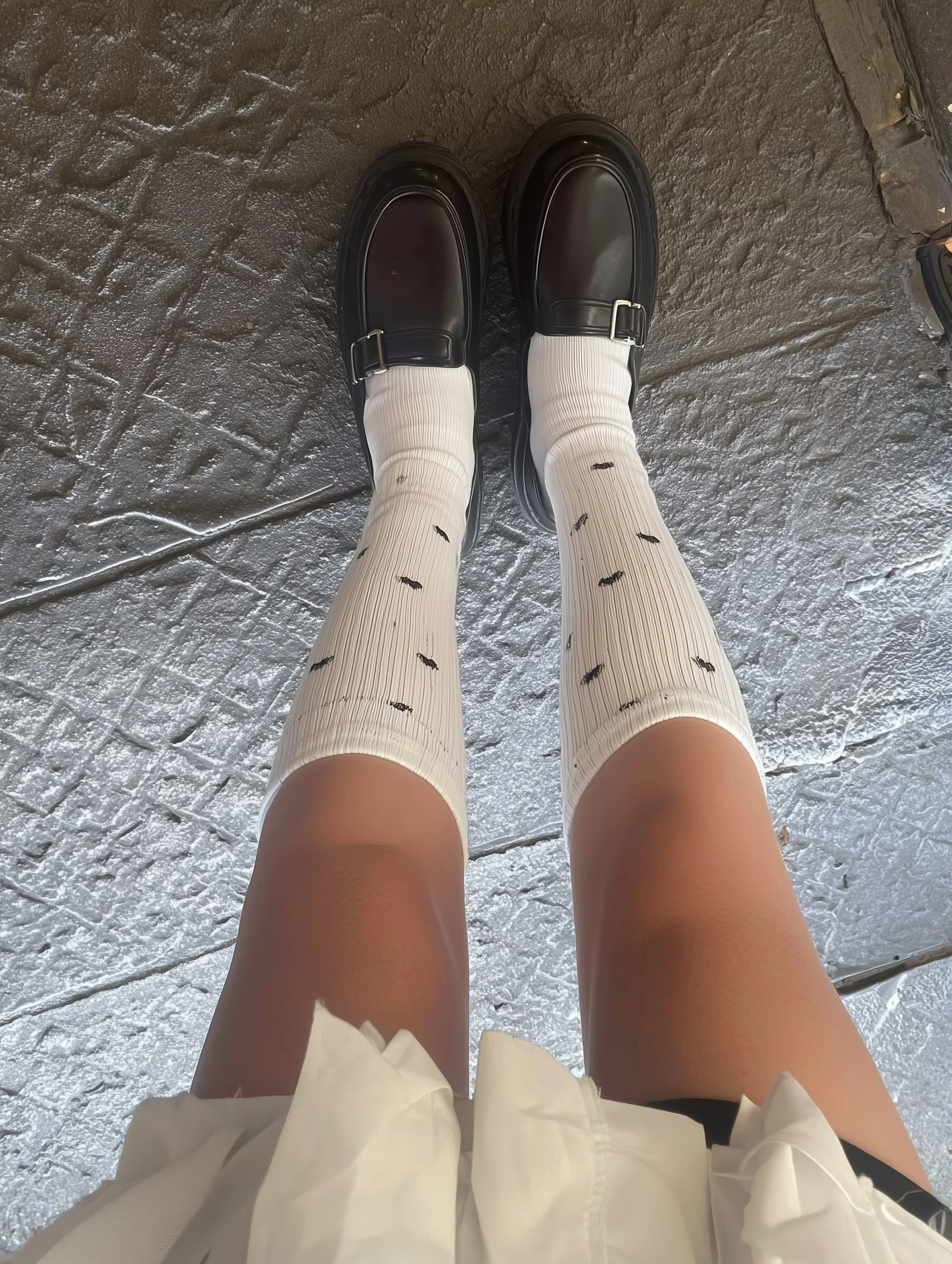 Phone photo of a pair of girl legs wearing high socks and black shoes from above