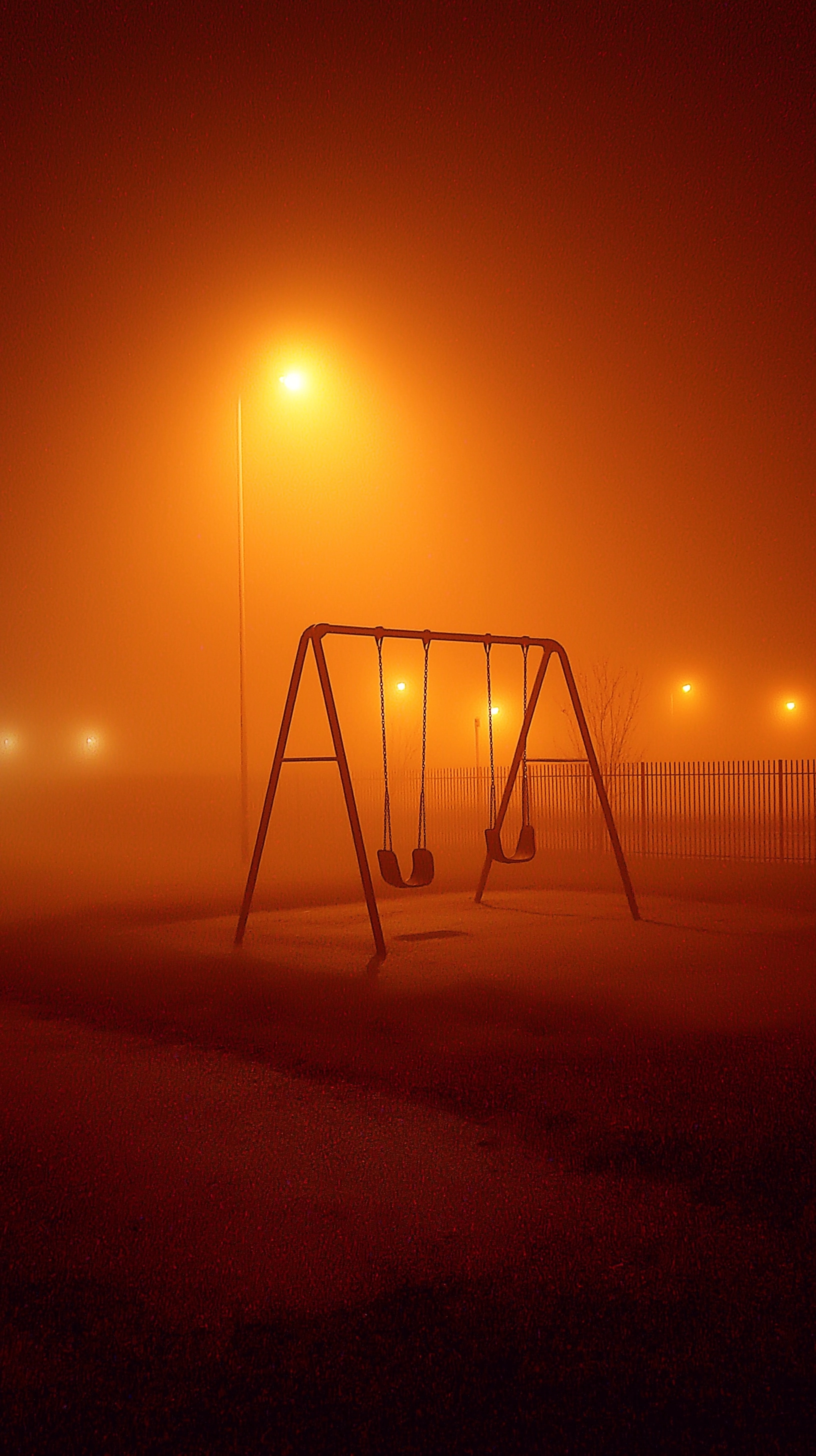 Photo-realistic liminal horror, old empty playground surrounded by fog, swings slightly tilted