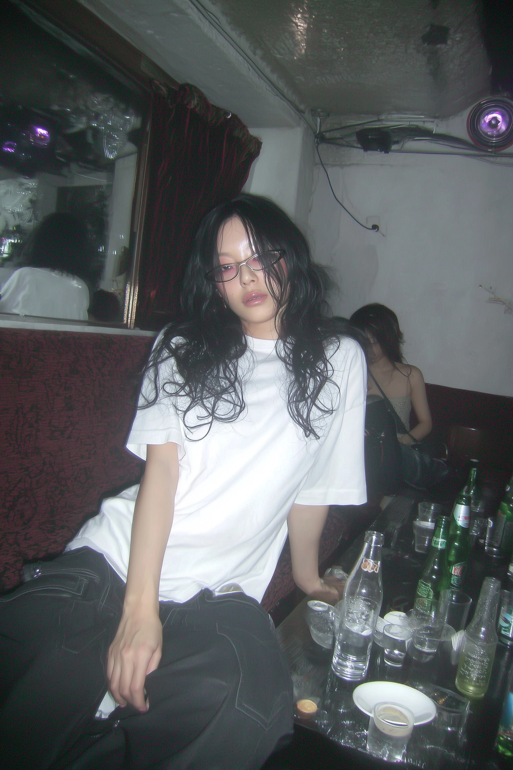 A candid flash photograph of an awkward nerdy Asian woman in her 20s with medium-length black curly