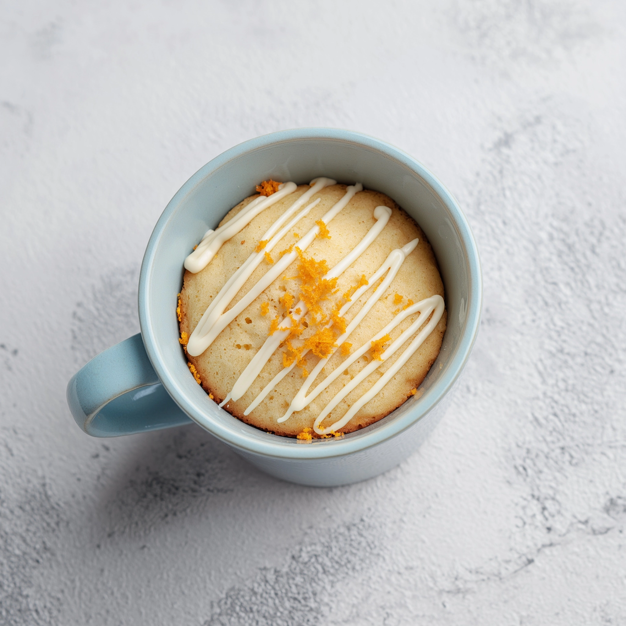 A bird's-eye view photograph of a warm, moist plain sponge mug cake in a modern light blue ceramic c