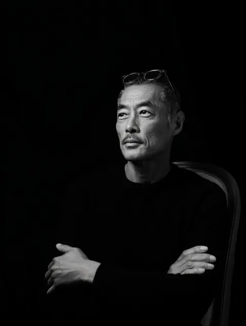A black-and-white portrait of an asian man with short hair, wearing glasses on his head