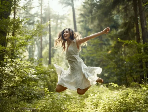 A Caucasian girl joyfully jumping in a lush forest, mid-air motion captured, expressive smile