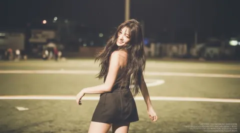 A photo of an asian woman in short skirt, smiling and dancing on the football field at night. she ha