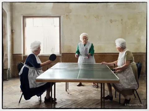 A realistic photography of three women playing a game named "sagouine pong"