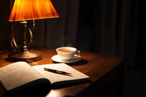 A high-end, elegant author's desk at night. A warm, amber-colored desk lamp illuminates an open note