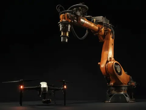 A robotic arm vs a modern drone for scale, black background