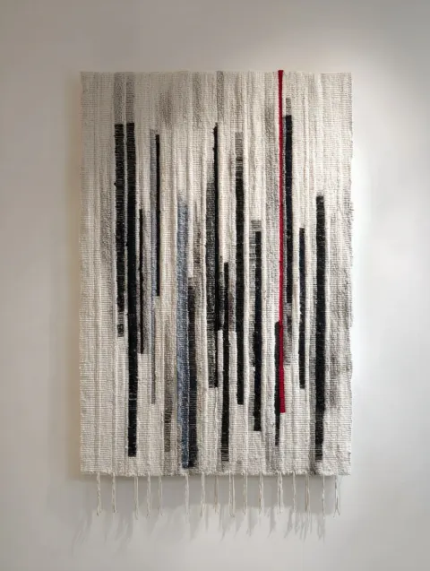 Textile art haning on teh wall, black and white, a tiny red and blue, elegant, no other object