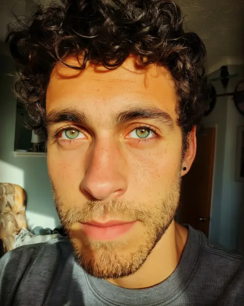 A photograph of an attractive mixed-race man, green eyes, and a stubble beard