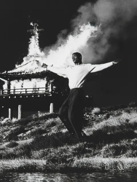 A man on a hillside with his arms in the shape of a cross
