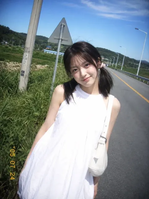 A young East Asian girl in her early 20s is on a rural highway. Side