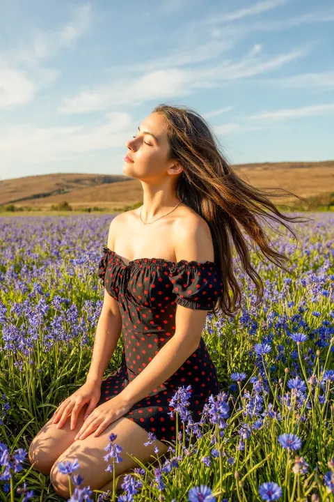 Medium Full Shot (kneeling) of a Young Woman with Long, Windblown Hair in a Wildflower Field