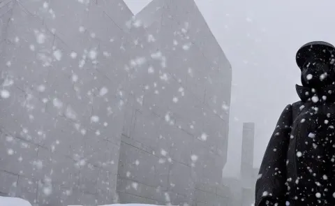 Black and White Photo of Snow Falling on a White Statue Wearing a Puffer Jacket