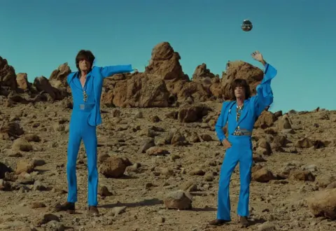 Mick Jagger Dressed in Blue Costume with Jewels in a Dry Rocky Desert Landscape