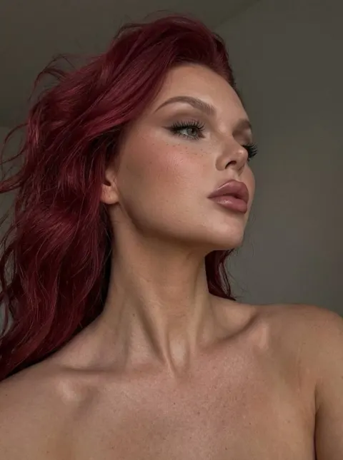 A woman with wavy red hair and freckles looking to the side.
