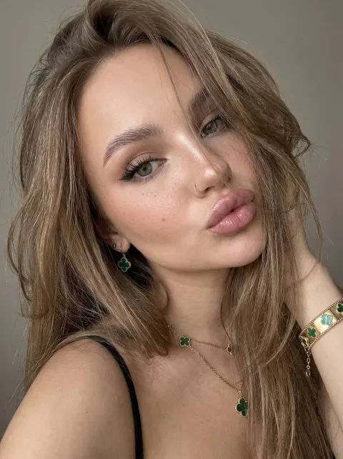 Close up portrait of a woman with blonde hair, green eyes, and freckles wearing green clover jewelry.