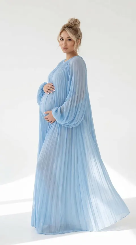 A pregnant woman with blonde hair in a bun wearing a long light blue pleated dress against a white background.
