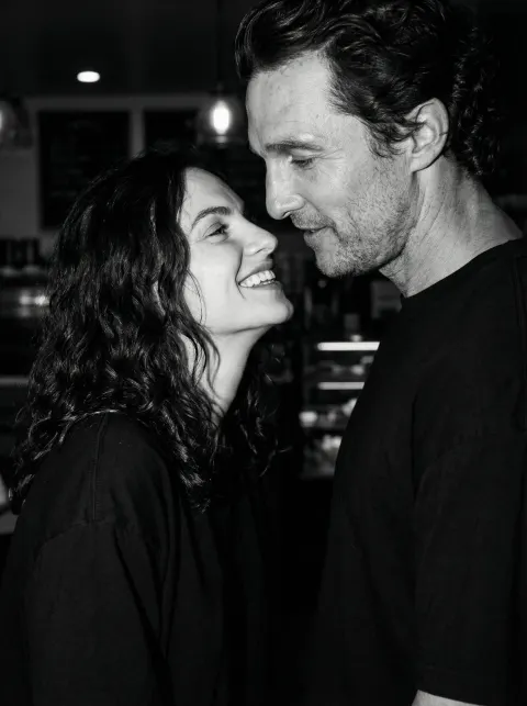 A black and white close-up of a woman smiling at a man in an indoor setting.