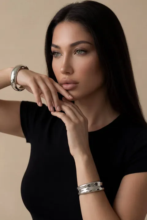 A woman with long dark hair wearing a black fitted top poses in front of a neutral background.