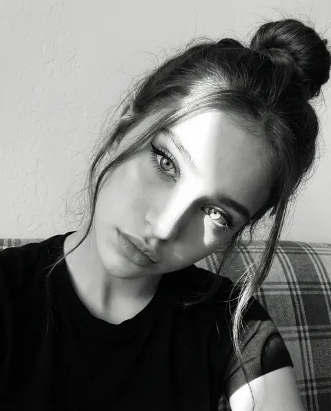 A woman wearing a black t-shirt sits on a checkered sofa against a plain light wall.