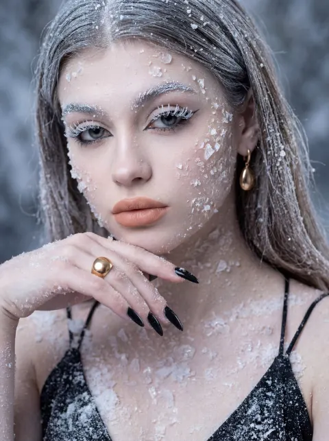 A woman with long gray hair wearing a black top is covered in white ice crystals and snow.