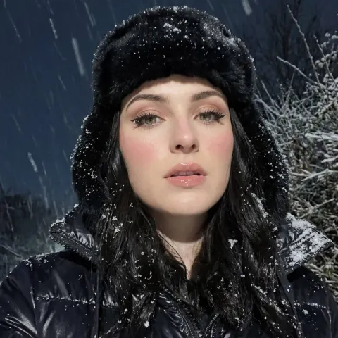 A woman wearing a black fur hat and puffer jacket stands outdoors during heavy snowfall.