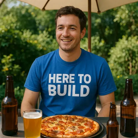 Person Wearing a Blue "Here to Build" Shirt Sits Outdoors