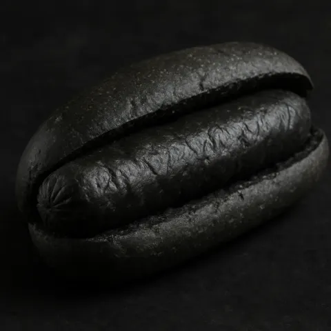 Dark Bun Holding a Sausage That Is Charcoal-gray in Color
