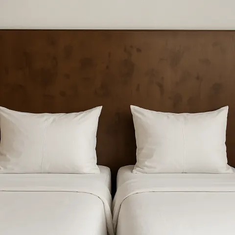 Two Beds with White Pillows and a Brown Wooden Headboard
