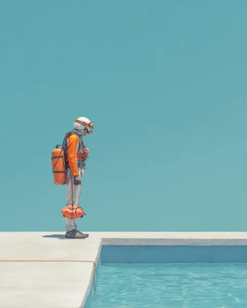 A person standing at the edge of a diving board, fully equipped with helmet, life jacket