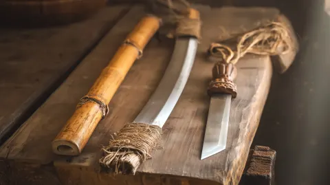 A photorealistic product shot of three Tang Dynasty blades arranged on a rough wooden workbench in a