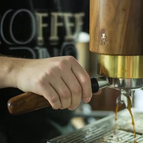 A close-up of someone holding an espresso machine and making coffee with the "coffee pn" design in t