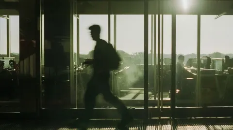Documentary photograph, a person walking through a glass door into a building, motion blur