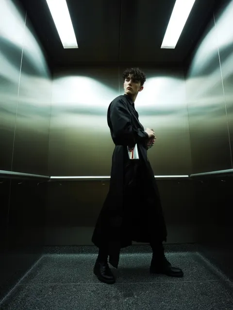 High fashion editorial photograph, androgynous model inside a sterile stainless steel elevator