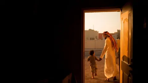 Editorial documentary photograph, a Saudi Arabian father in casual traditional white thobe arriving