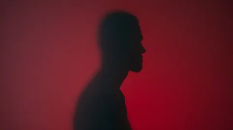 Shadow-like human form behind translucent surface, smooth head with no facial features, no hair