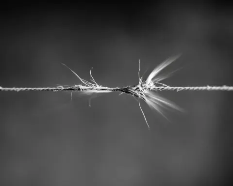 Black and white surreal close-up of a taut thread stretched across the frame snapping mid-air