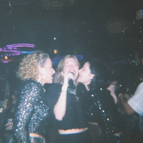 Documentary style nightlife photo of a group of female friends in their 30's singing together in a m