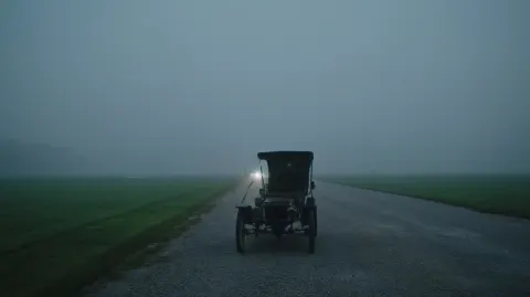 Extreme close-up side view of a vintage 1910s carriage-style automobile (thin spoked wheels