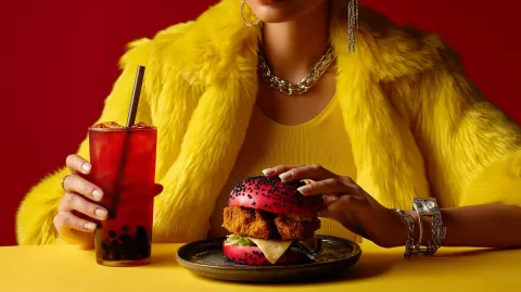 Over-the-top close-up of a crispy chicken burger with a vibrant red bun topped with black and white