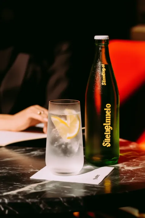A chilled glass of sparkling water with ice and fresh lemon slices on a dark marble restaurant table