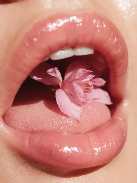 Macro photo of a pink orchid flower lying in the back of the mouth on the girl's tongue. the flower