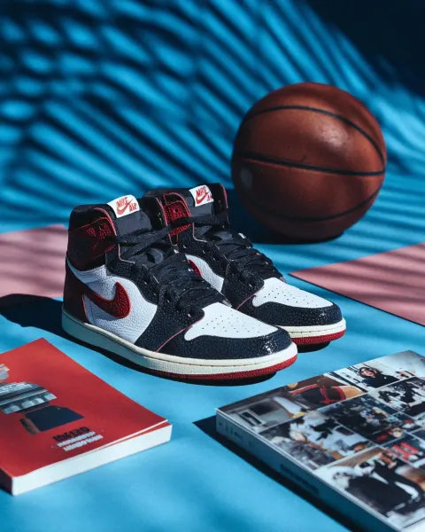 A pair of black and red retro jordan shoes, a basketball on the ground with a poster and playbook ne