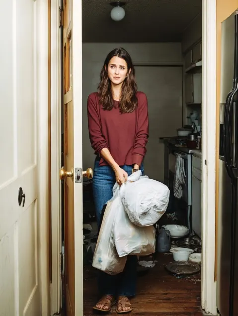 Woman holding grocery bags entering messy kitchen, exhausted expression