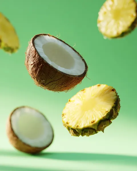Isolated realistic pineapple and coconut slices floating against a light green wall on background. B