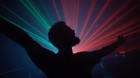 Photograph of a silluate of bearded man dancing in front of laser lights in a dark room