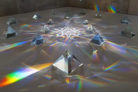 A series of glass pyramids and prisms are arranged in a large geometric pattern. A spotlight from th