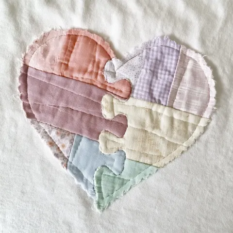 A soft pastel patchwork heart applique made from layered fabric pieces